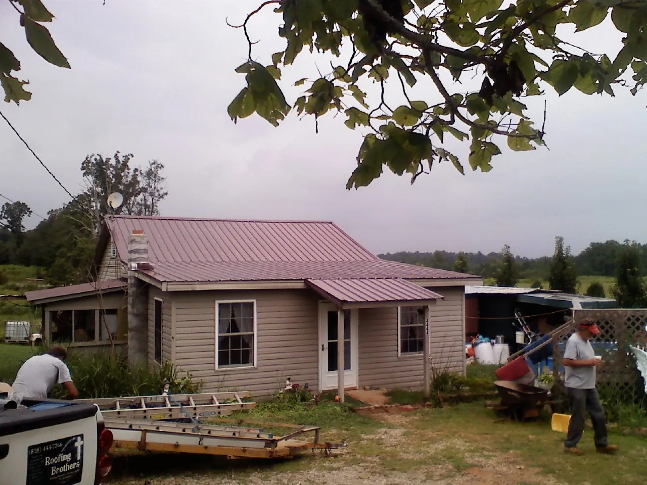 Crew finishing a mauve metal roof on a small farmhouse in Seminole